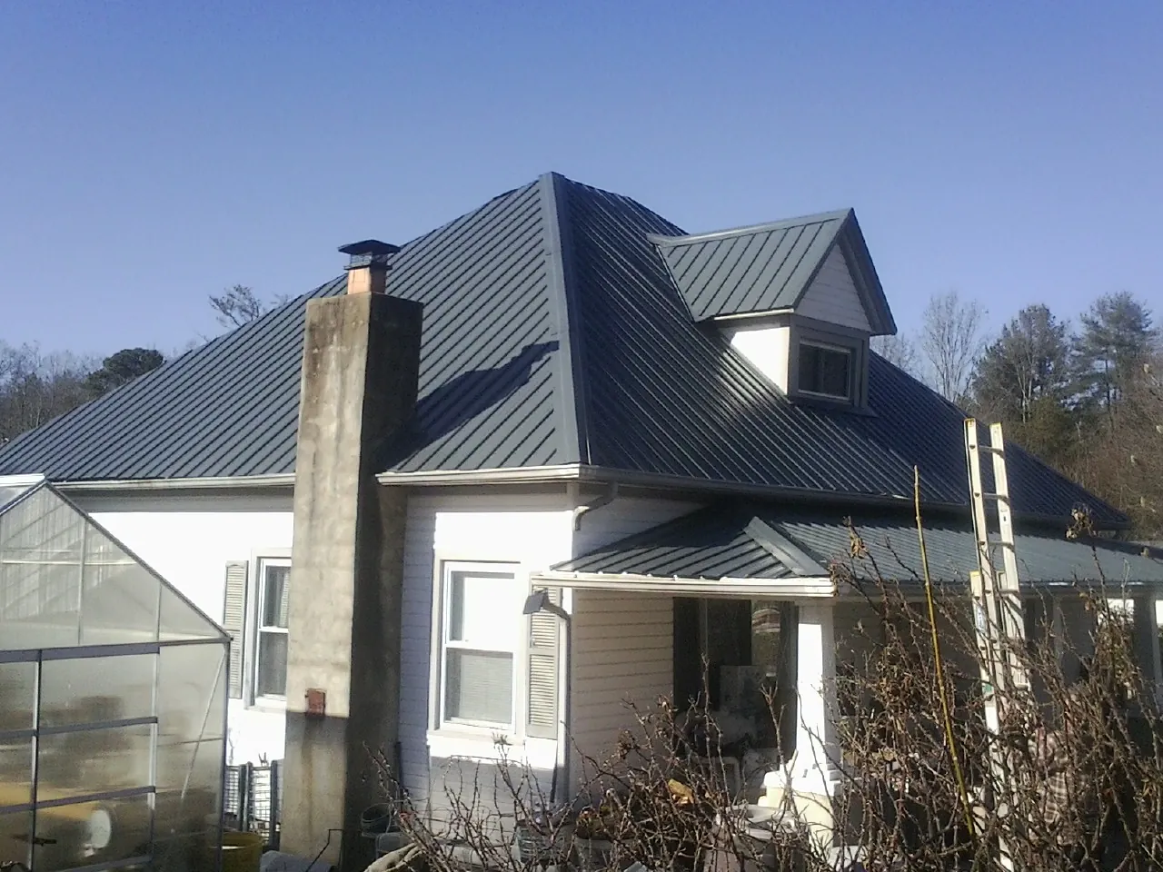 Dark blue standing seam metal roof on a white farmhouse with dormer — Slate & Tile Roof Repair by Roofing Brothers in Spirit Lake