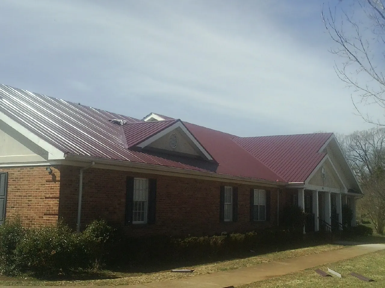 Red metal roof with gabled entries on a long brick building, from a Hail Damage Roof Repair job in Spirit Lake