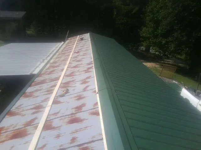 Old rusted panels beside newly installed green metal roofing — Wind Damage Roof Repair by Roofing Brothers in Spirit Lake