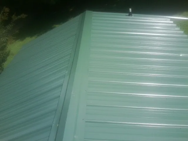 New green metal panels meeting at the ridge of a roof — Flat Roof Repair work by our crew in Spirit Lake