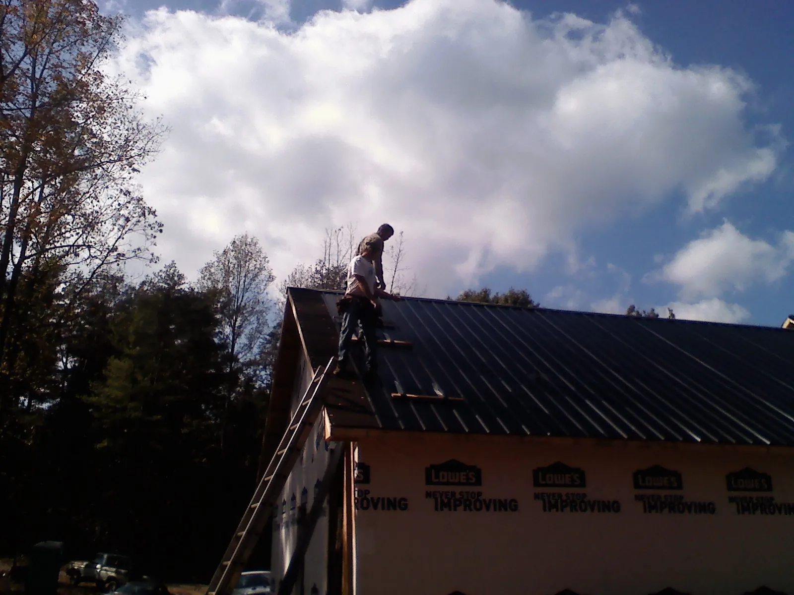 Roofer fastening dark metal panels high against a cloudy sky, from a Roof Inspection job in Spirit Lake