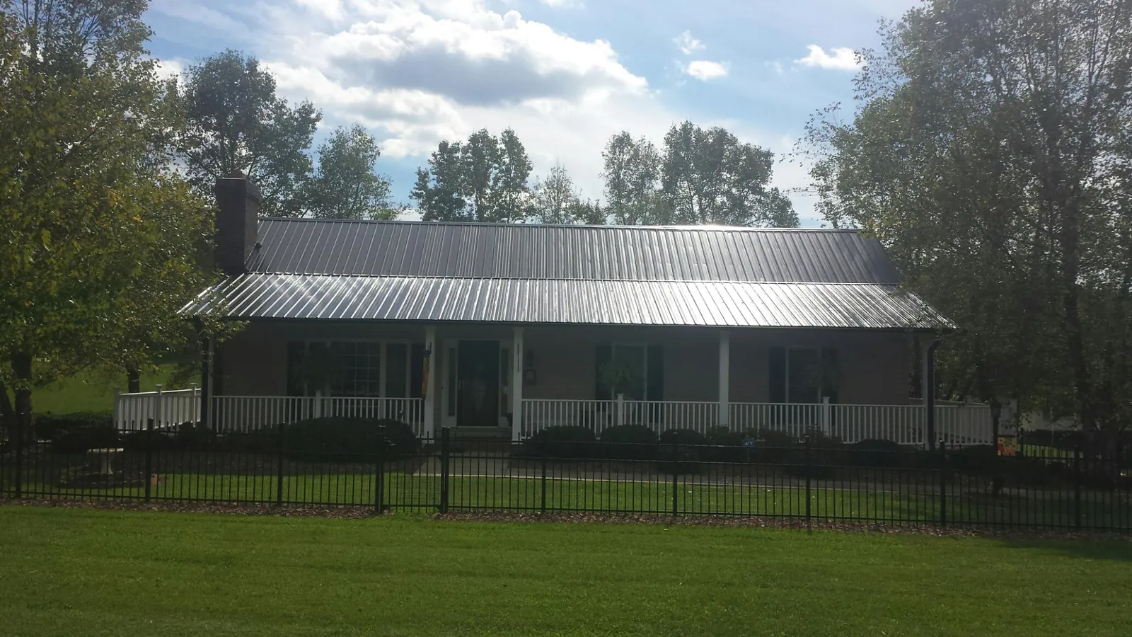 Gray metal roof on a brick ranch with a full width front porch — Gutter Guard Installation work by our crew in Spirit Lake