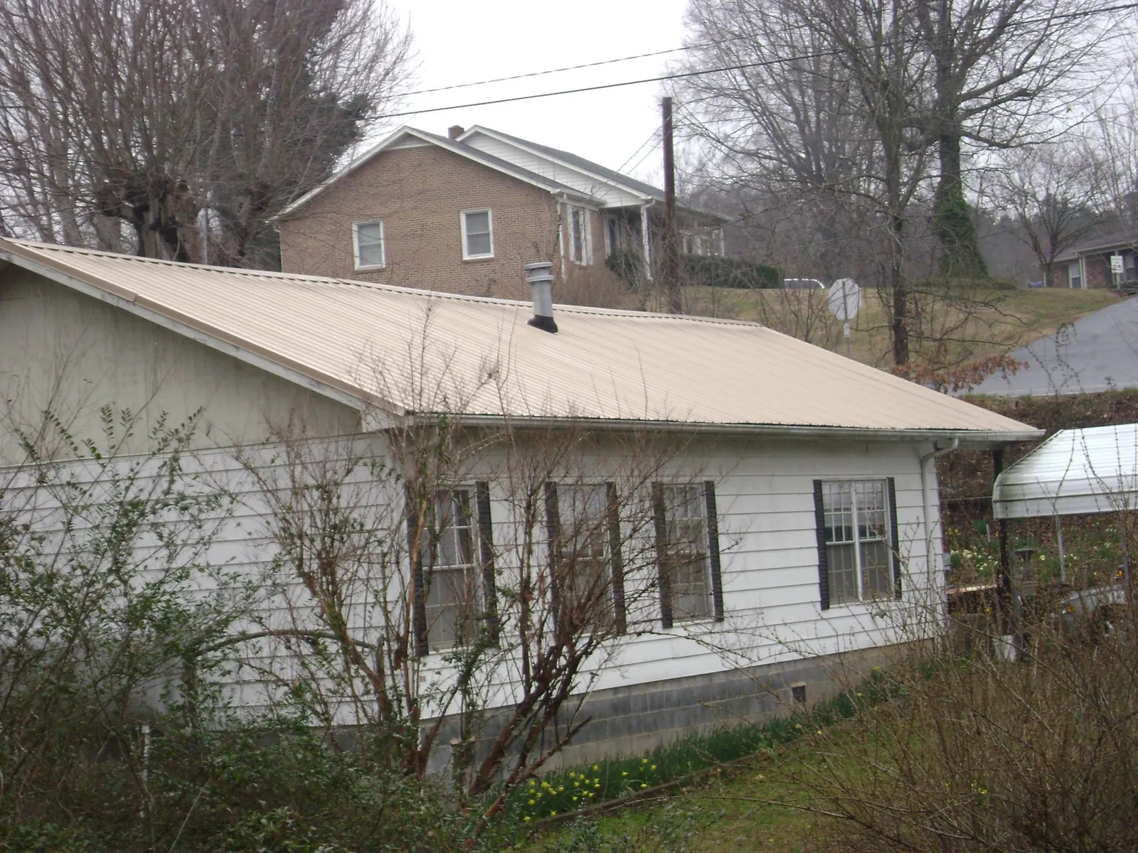 Tan metal roof on a white sided house set into a hillside — Commercial Roofing by Roofing Brothers in Spirit Lake