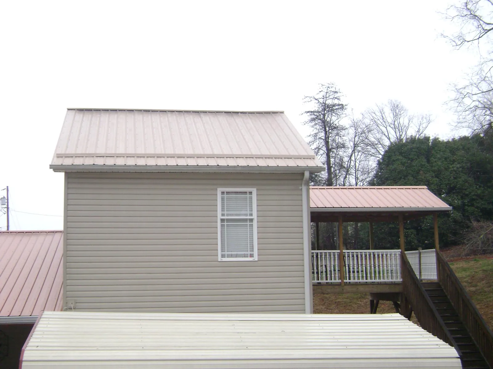 Tan metal roofs on a two story addition and attached porch, from a Roof Replacement job in Spirit Lake