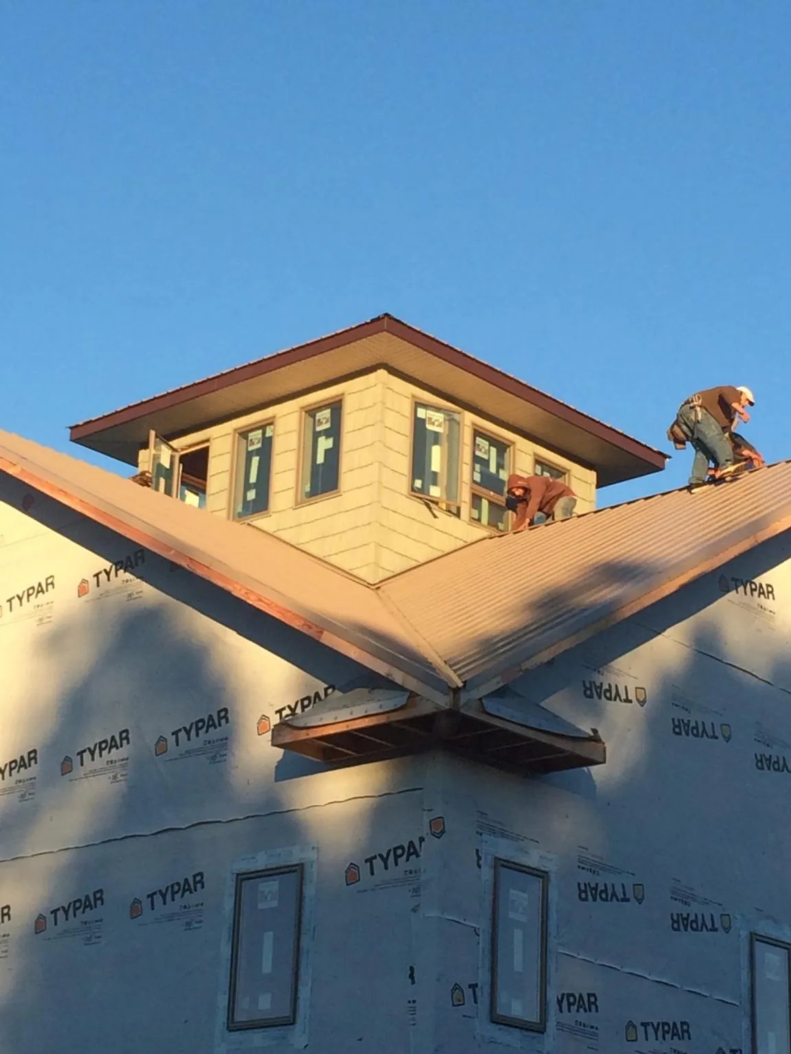 Roofers working around a rooftop cupola on a new metal roof at sunset — Roof Waterproofing in Spirit Lake by Roofing Brothers